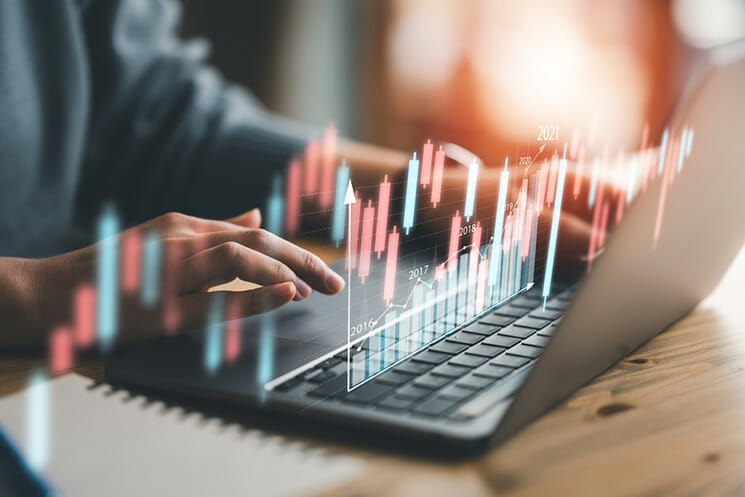 A concept image showing a financial graph superimposed over a funded trader using a laptop computer.