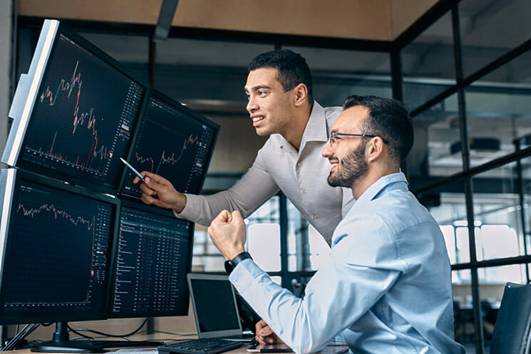 Two funded traders at desk in office looking at candlestick chart and celebrating a profit gain on stock market