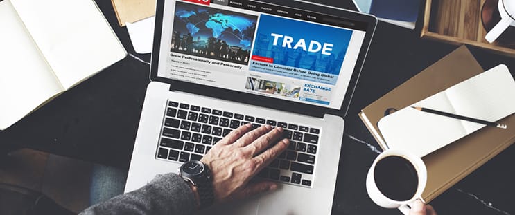 Day trader reading news on laptop on table with coffee cup and notebook for making trade analysis