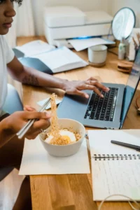 Person eating instant noodles while looking at laptop.