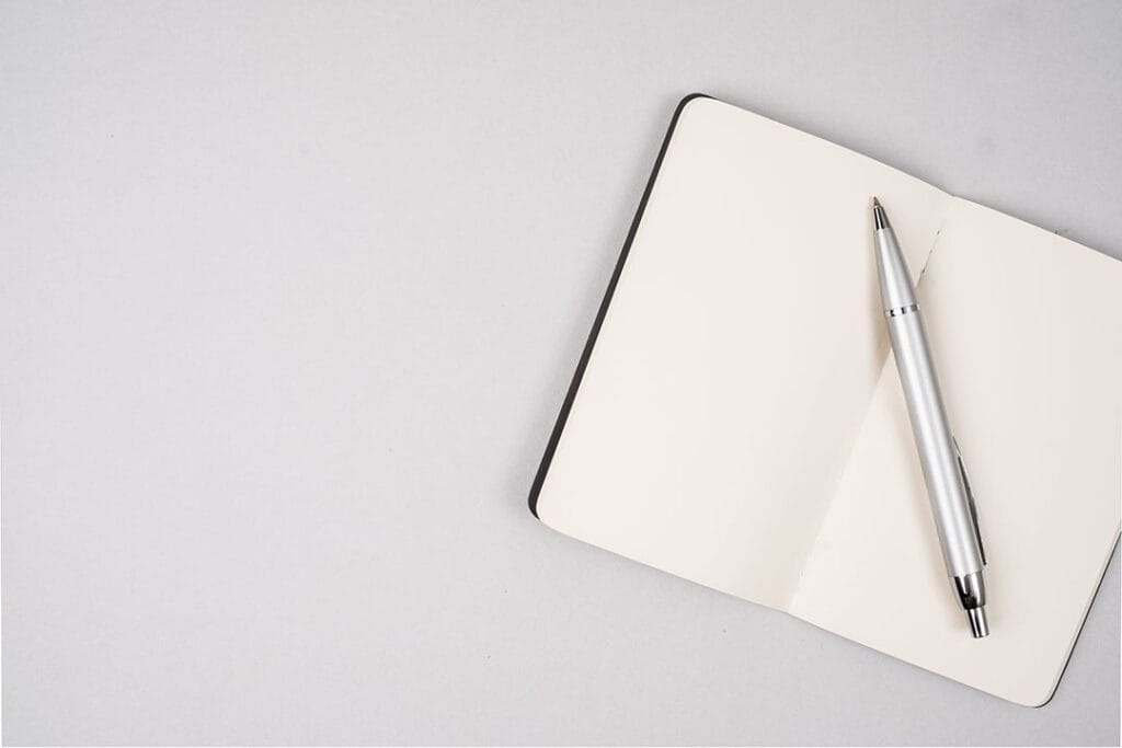 A silver pen rests on an empty, open, day trading journal on a white background.