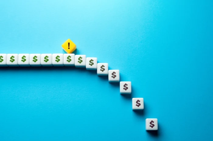 Concept of losing money illustrated by a line of dice with U.S. dollar signs with some dice falling away and a yellow diamond with an exclamation sign serving as a warning
