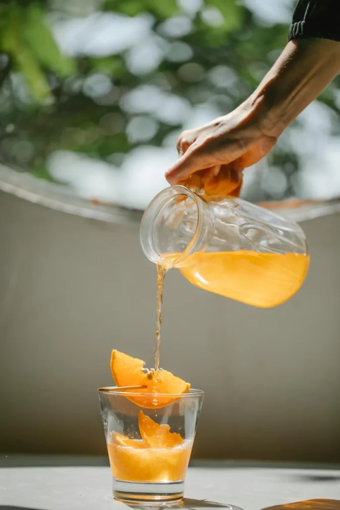 A hand pours a bright orange liquid from a glass pitcher into a glass containing orange slices representing forex liquidity.