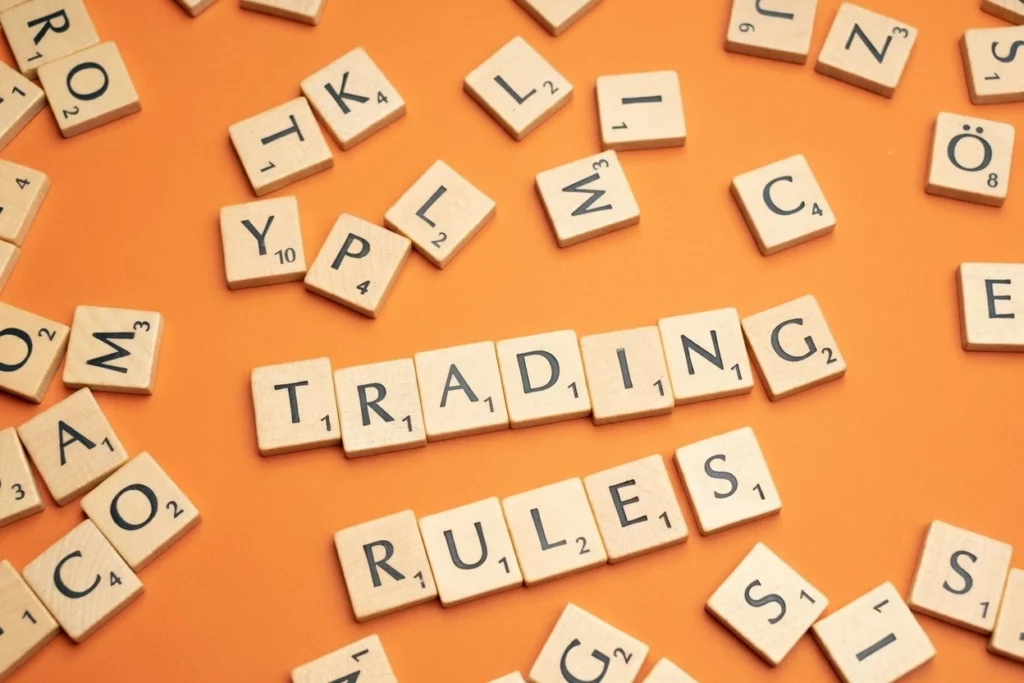 Scrabble tiles arranged on an orange background spelling "TRADING RULES" with scattered letters around them.