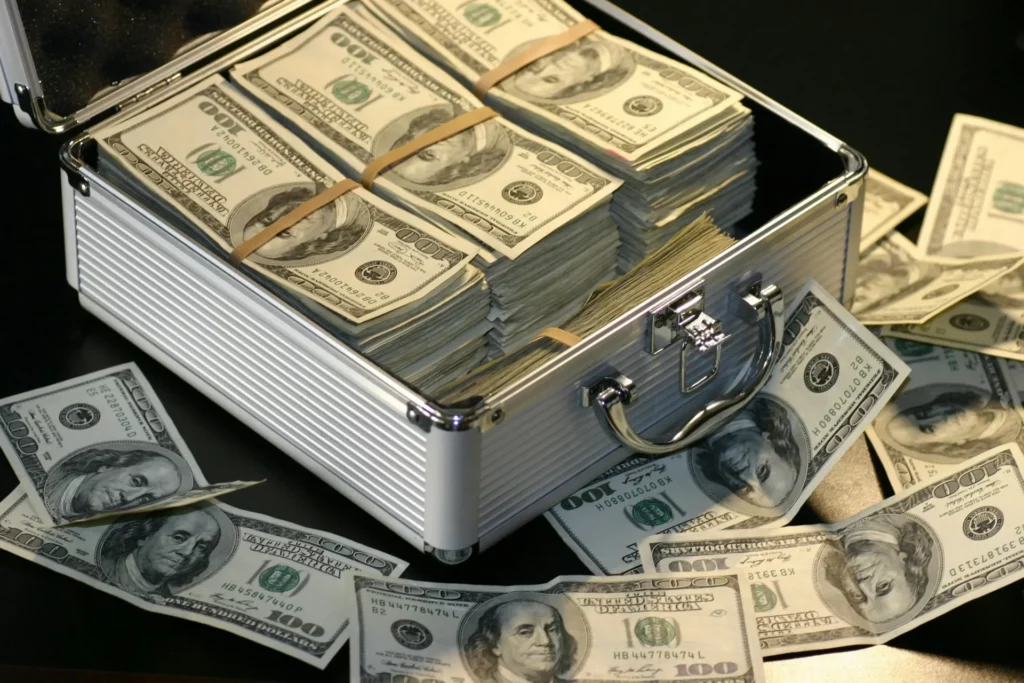 Open silver briefcase overflowing with stacks of $100 US dollar bills - cash and fiat currency as one of the best assets to trade.