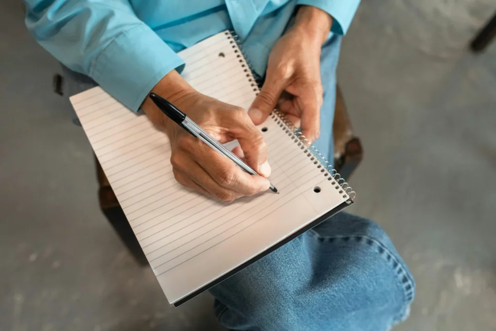 Hands writing in notebook for trading plan to prevent prop firm trading mistakes. 
