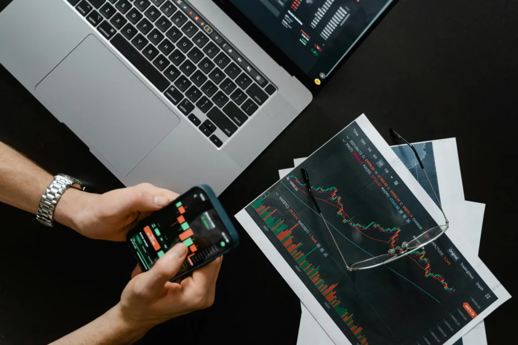 Person analyzing crypto charts on a laptop and smartphone, illustrating what are prediction markets and how traders forecast the future. 